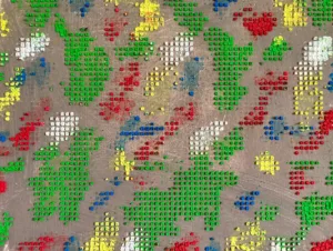 Physical Pixel Abstract Pattern Composition In Blue Green Red White And Yellow — abstract oil-and-wax painting; raised square dots of green, red, yellow, blue and white forming a pixel pattern on a warm gray ground — detail 1 of 3, close-up of surface texture