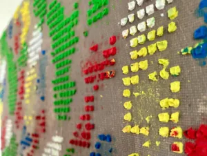 Physical Pixel Abstract Pattern Composition In Blue Green Red White And Yellow — abstract oil-and-wax painting; raised square dots of green, red, yellow, blue and white forming a pixel pattern on a warm gray ground — detail 2 of 3, close-up of surface texture