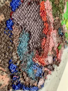 Physical Pixel Portrait Male Side Profile — grid-based oil-and-wax portrait; a man's head in profile built from raised square pixels in green, pink, gray, blue and brown on a pale gray ground — detail 2 of 2, close-up of surface texture