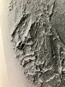 Tactile Relief Portrait Of A Male In Black And White — monochrome oil, wax and spray paint relief; a three-quarter male head in thick sculpted impasto under an even gray spray gradient — detail 1 of 2, close-up of surface texture