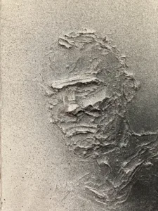 Tactile Relief Portrait Of A Male In Black And White — monochrome oil, wax and spray paint relief; a three-quarter male head in thick sculpted impasto under an even gray spray gradient — detail 2 of 2, close-up of surface texture