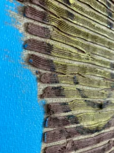 Tactile Texture Linear Squeeze Portrait Smiley Face — oil-and-wax relief portrait; a brown striped head with a flat yellow smiley face, on turquoise — detail 2 of 3, close-up of surface texture